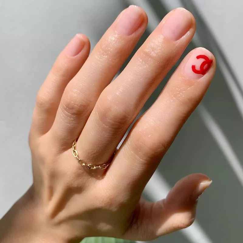 Minimalistische Maniküre mit roten Akzentnägeln mit Chanel-Symbol